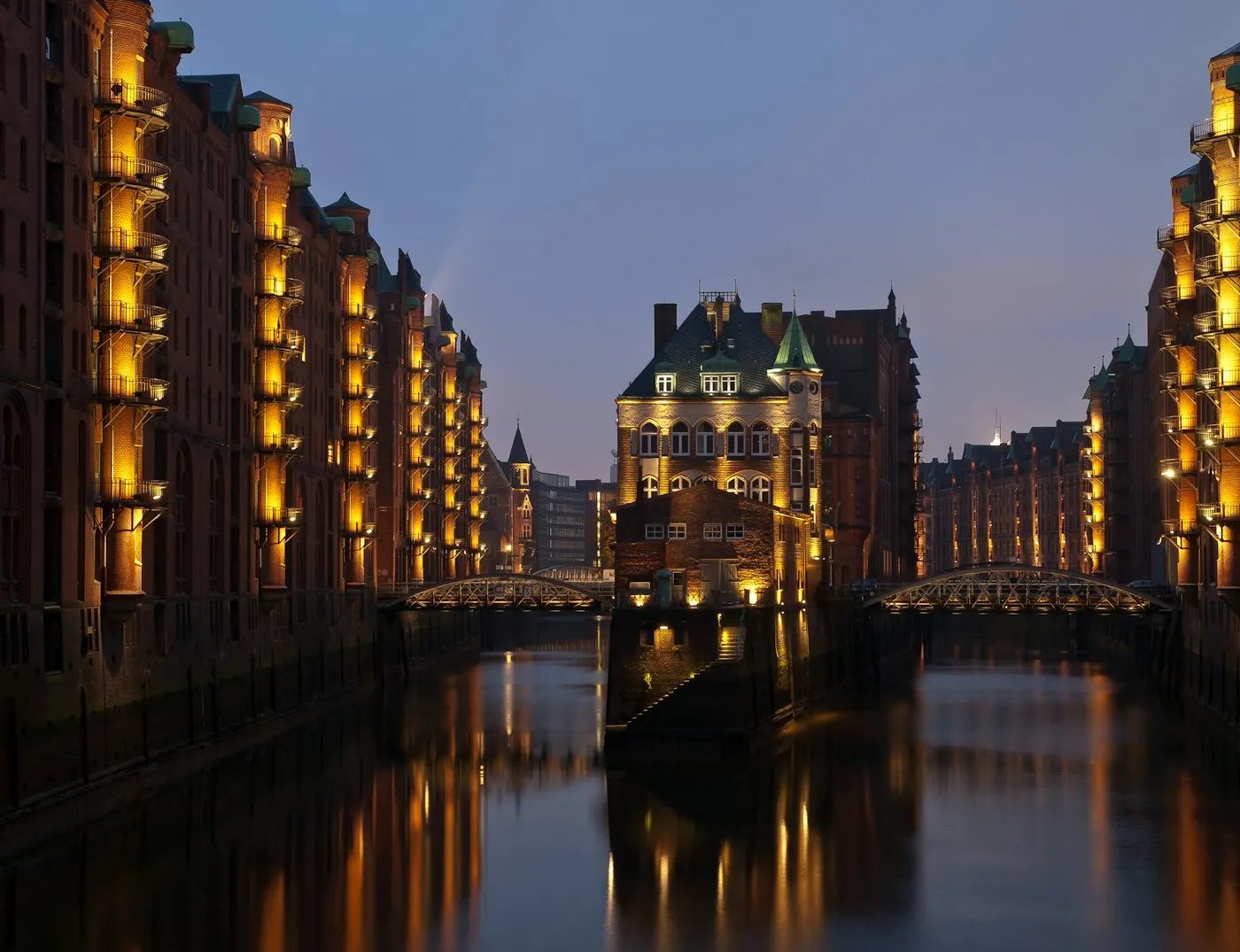 Hamburger Speicherstadt bei Nacht — dunkle Backsteinmauern und stilles Wasser im Fleet